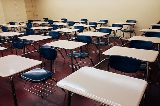 Aula de clase con mesas blancas y sillas azules.